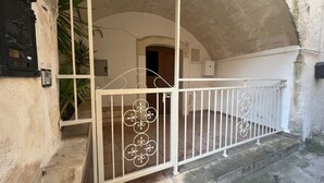 A white metal gate with decorative patterns, leading to a stone staircase and an arched doorway.