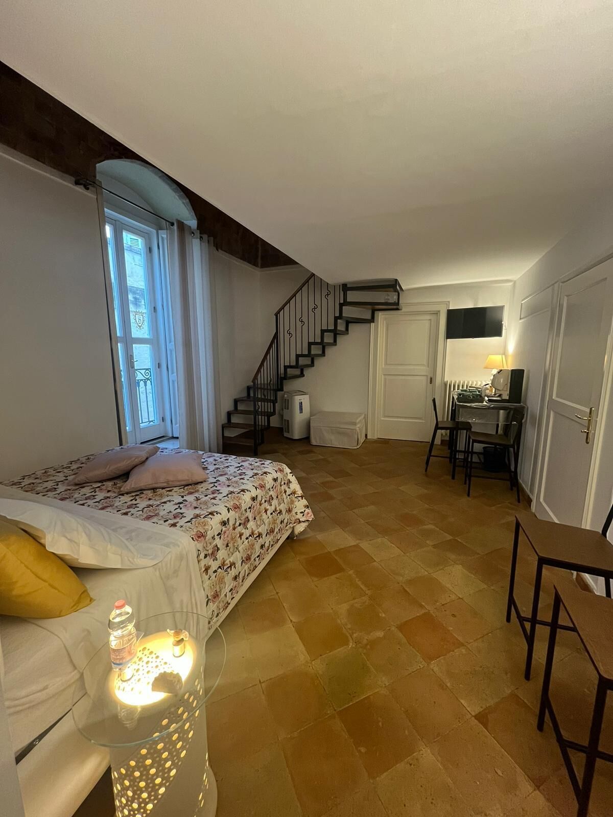 A bedroom with a bed, a desk, and a staircase leading to another room.