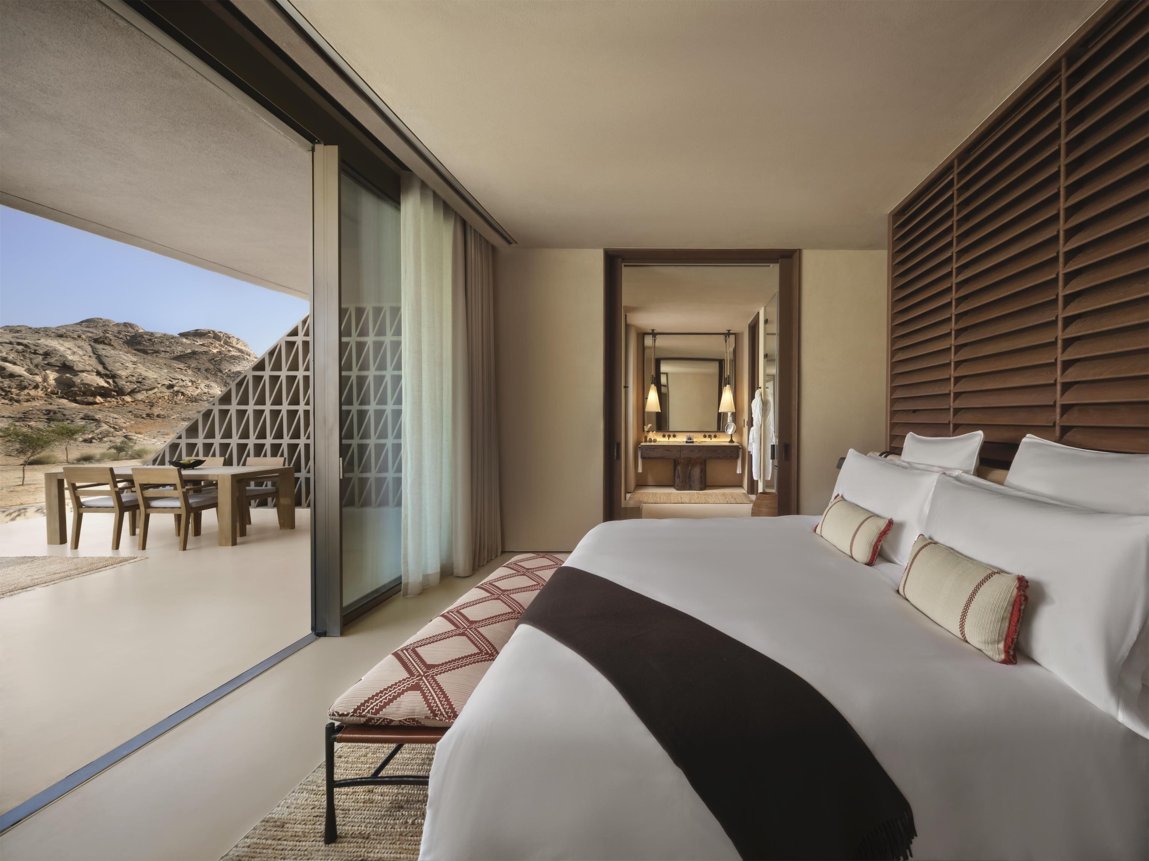 Une chambre d’hôtel moderne dotée d’un grand lit, d’une salle de bain avec un miroir et des serviettes, et d’un coin repas avec une table et des chaises.