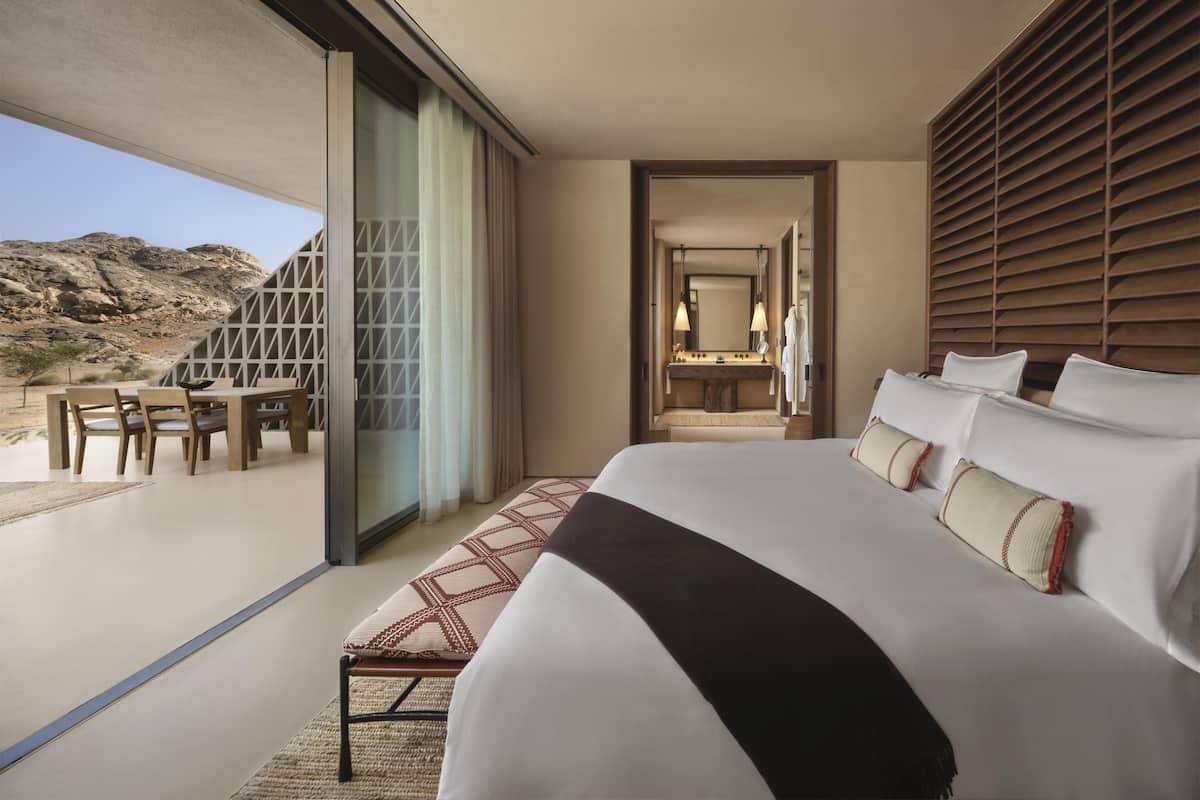 A modern hotel room with a large bed, a bathroom with a mirror and towel, and a dining area with a table and chairs.