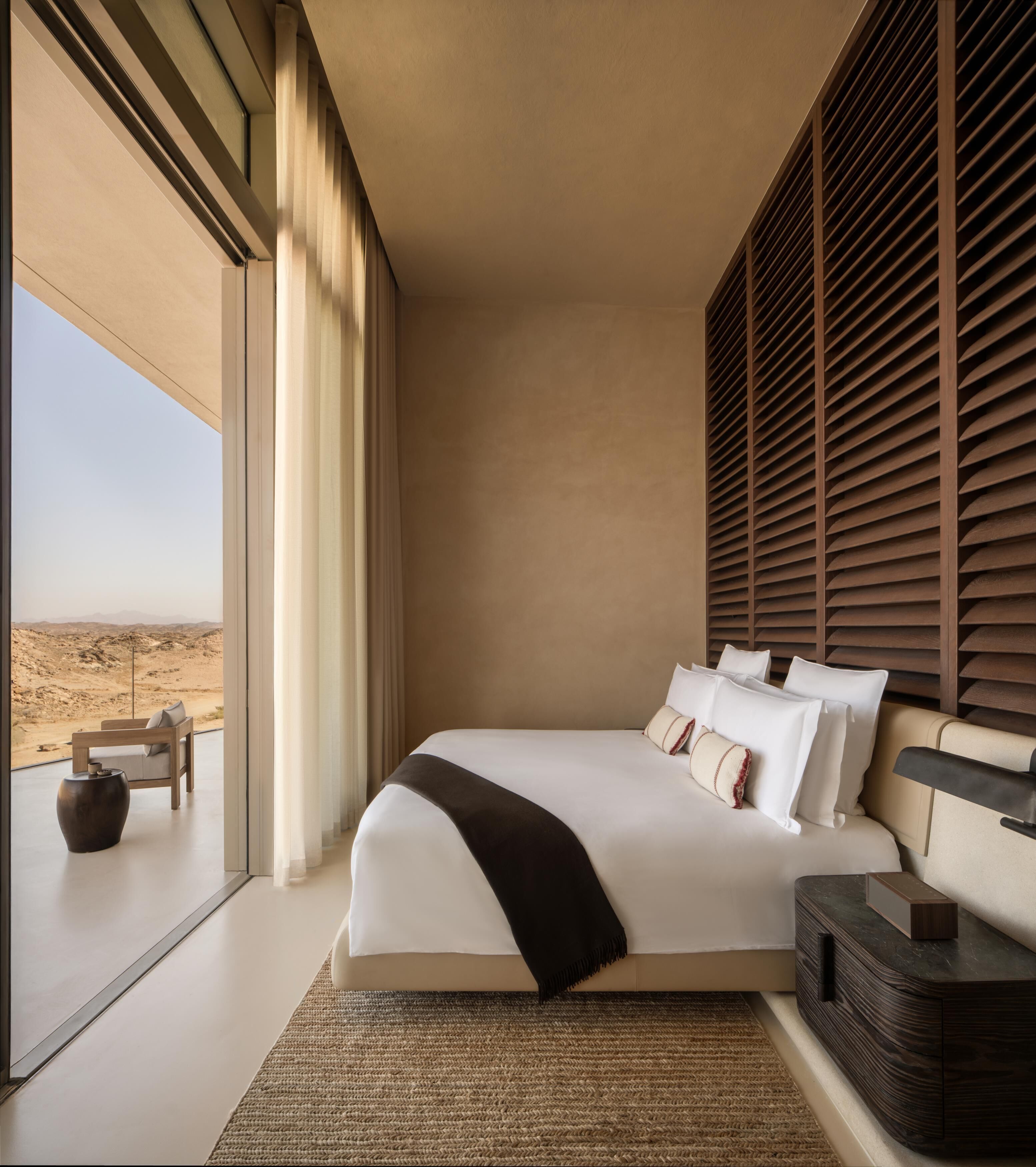 A bedroom with a large bed, a view of the desert, and a window with blinds.