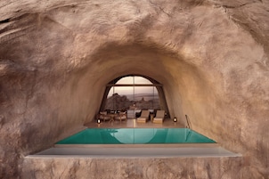 Un espacio con forma de arco que ofrece vistas a una piscina, asientos y un paisaje montañoso.