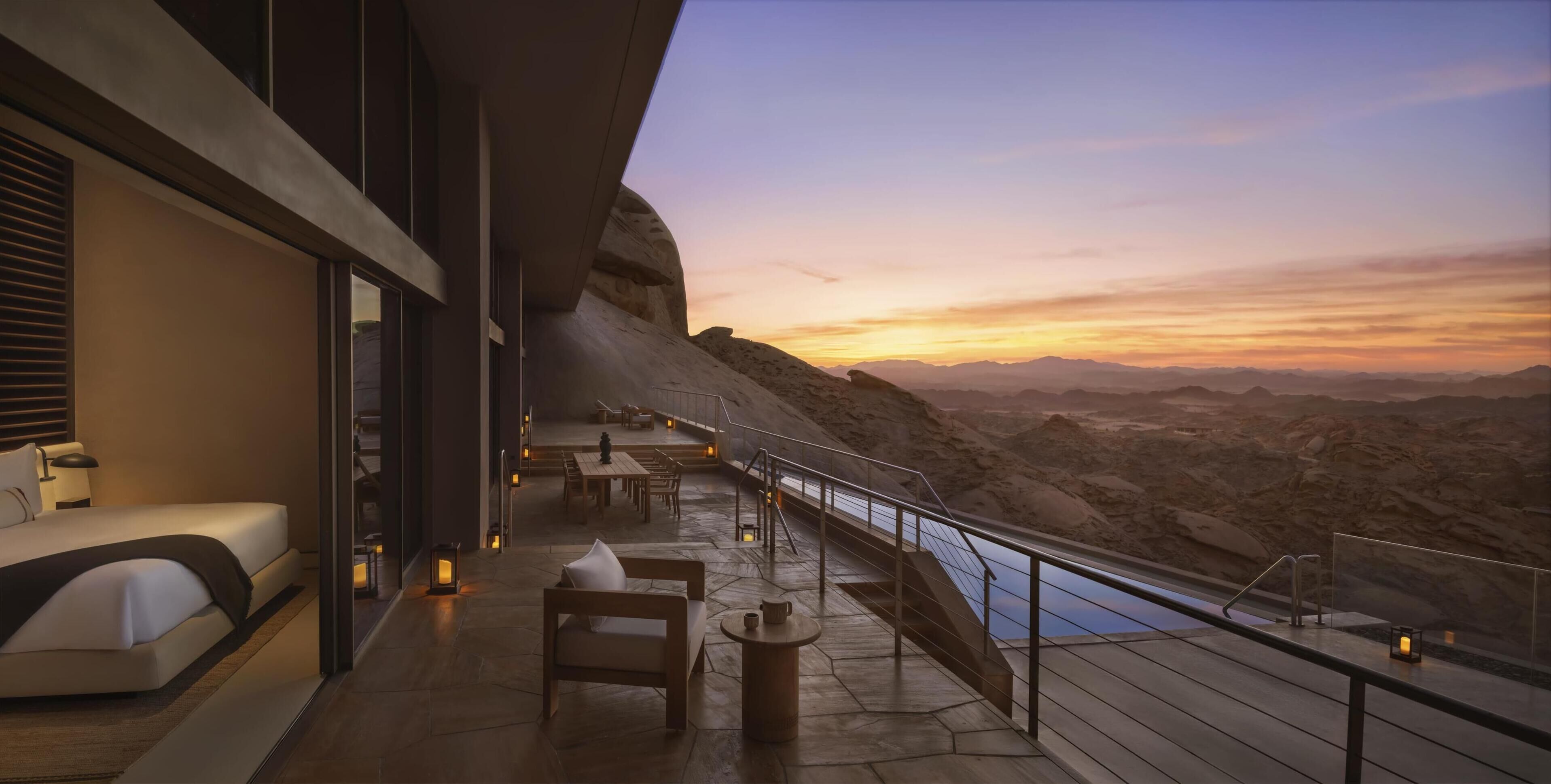 Una suite de hotel moderna con balcón que da a un paisaje desértico al atardecer.