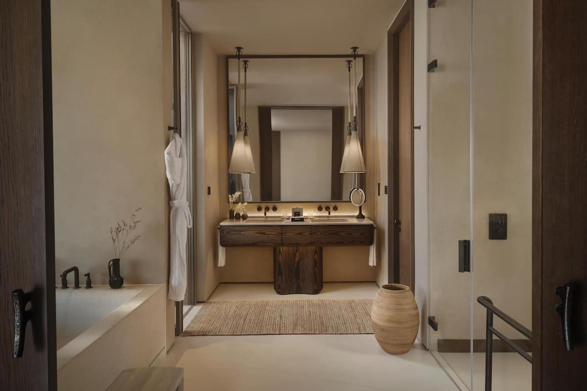 A modern bathroom with a large mirror, two pendant lights, a wooden vanity, a large vase, and a bathtub.