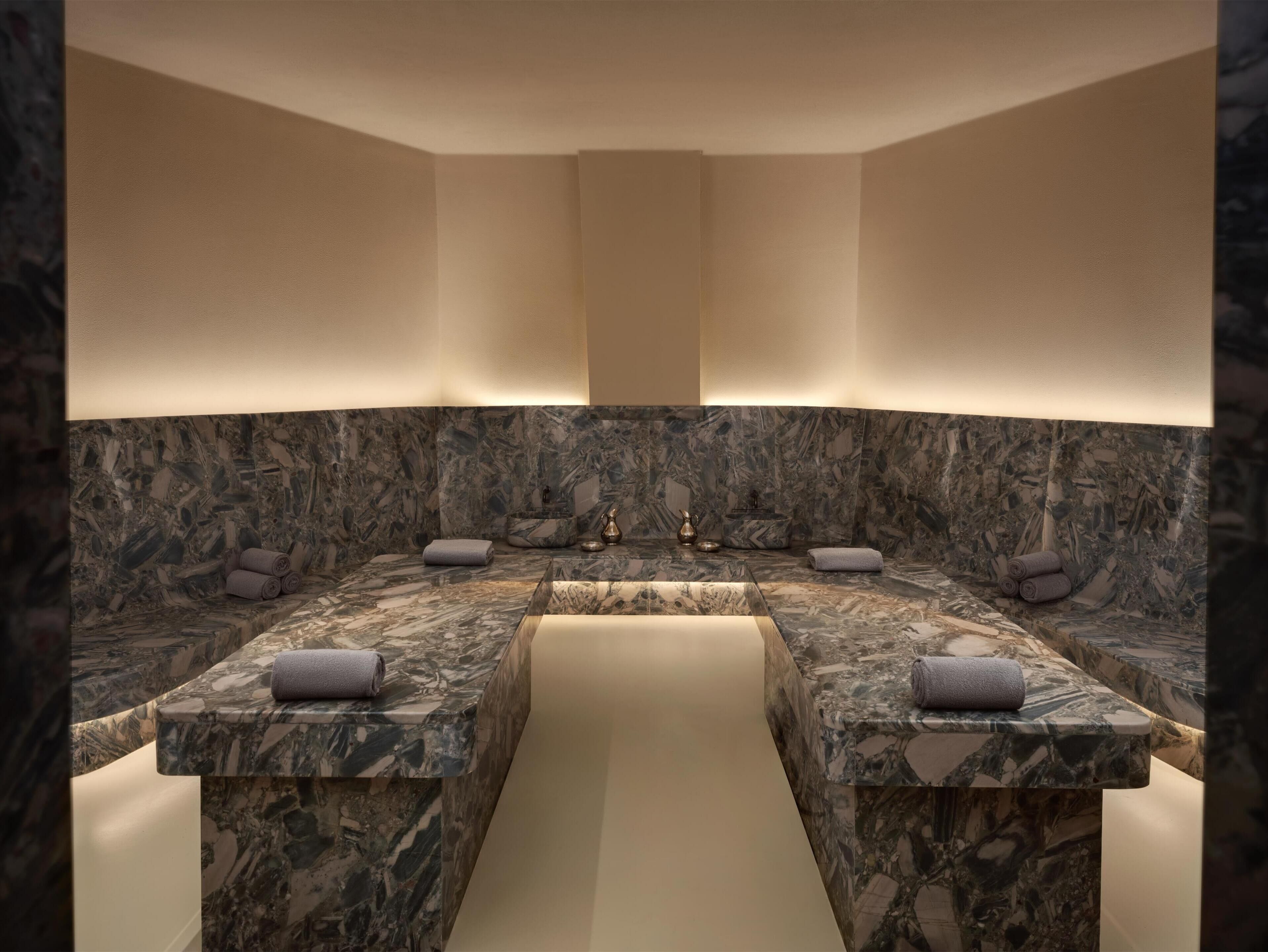 A modern bathroom with marble countertops, a central sink, and towels placed on the counters.