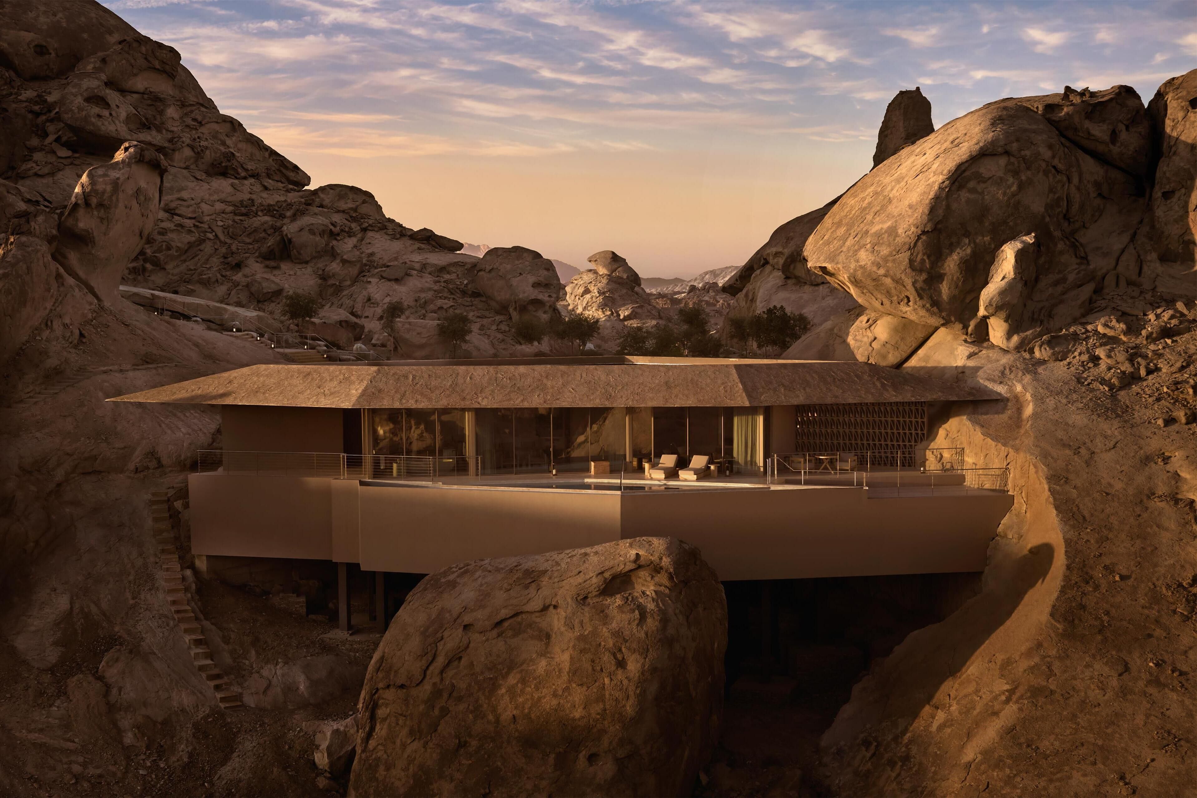 A modern building with a flat roof, large windows, and a balcony overlooking a rocky landscape.