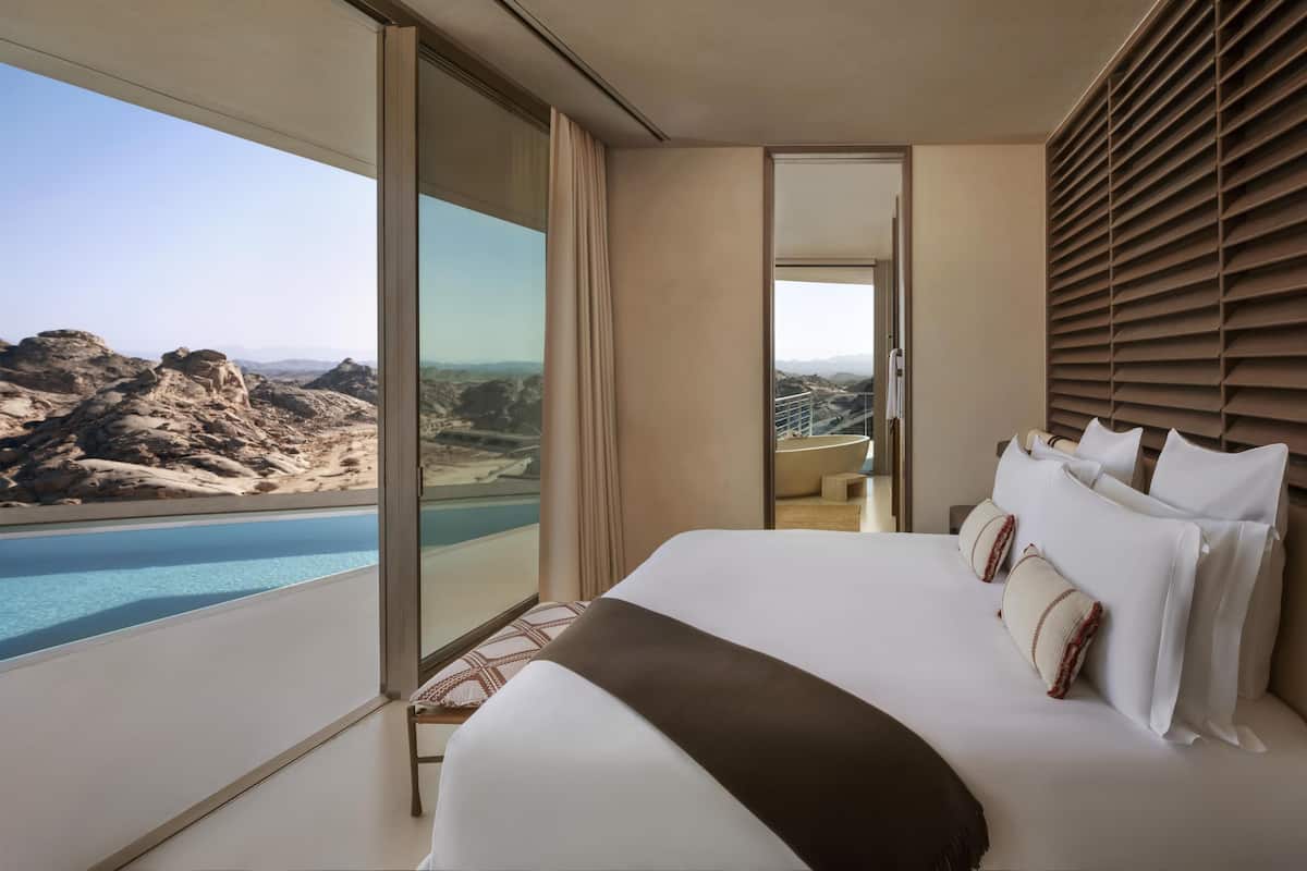 A modern bedroom with a large bed, a view of a mountainous landscape, and a large window.
