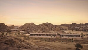 A desert resort with multiple modern villas, each with large windows and a flat roof, surrounded by rocky terrain and sparse vegetation.