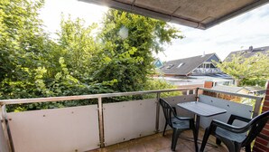 Un balcon avec une table et deux chaises, entouré d’une balustrade blanche et de verdure.