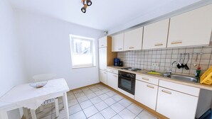 Une petite cuisine avec des meubles blancs, une table blanche et une fenêtre.