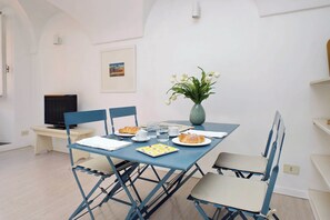 A dining area with a blue table, chairs, a vase with flowers, and a television on a stand. - Cimarra Apartment (Rome)