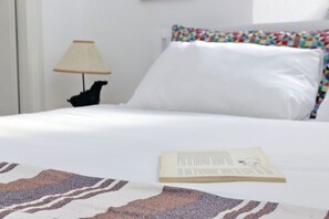 A neatly made bed with a white sheet, a colorful pillow, and a book on the bed. - Cimarra Apartment (Rome)