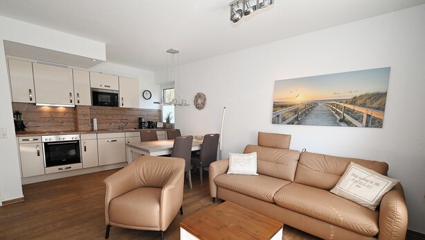 A modern living room with a beige sofa, a wooden coffee table, and a dining area with a table and chairs. - Fischer's Hus apartment 1<br>Beautiful apartment with terrace and access to the sea time (Büsum)