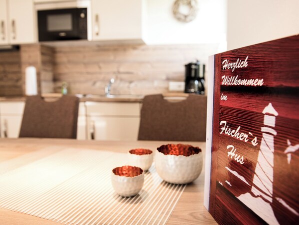 A wooden sign with text in a foreign language, a kitchen area with a microwave, and two bowls on a table. - Fischer's Hus apartment 1<br>Beautiful apartment with terrace and access to the sea time (Büsum)