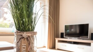 A glass jar with a rope handle and a wooden tag labeled "HOME" containing green grass, placed on a wooden table in a room with a TV and a white cabinet. - Fischer's Hus apartment 1<br>Beautiful apartment with terrace and access to the sea time (Büsum)