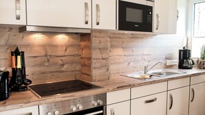 A modern kitchen with white cabinets, a stainless steel range, a microwave, and a coffee maker. - Fischer's Hus apartment 1<br>Beautiful apartment with terrace and access to the sea time (Büsum)