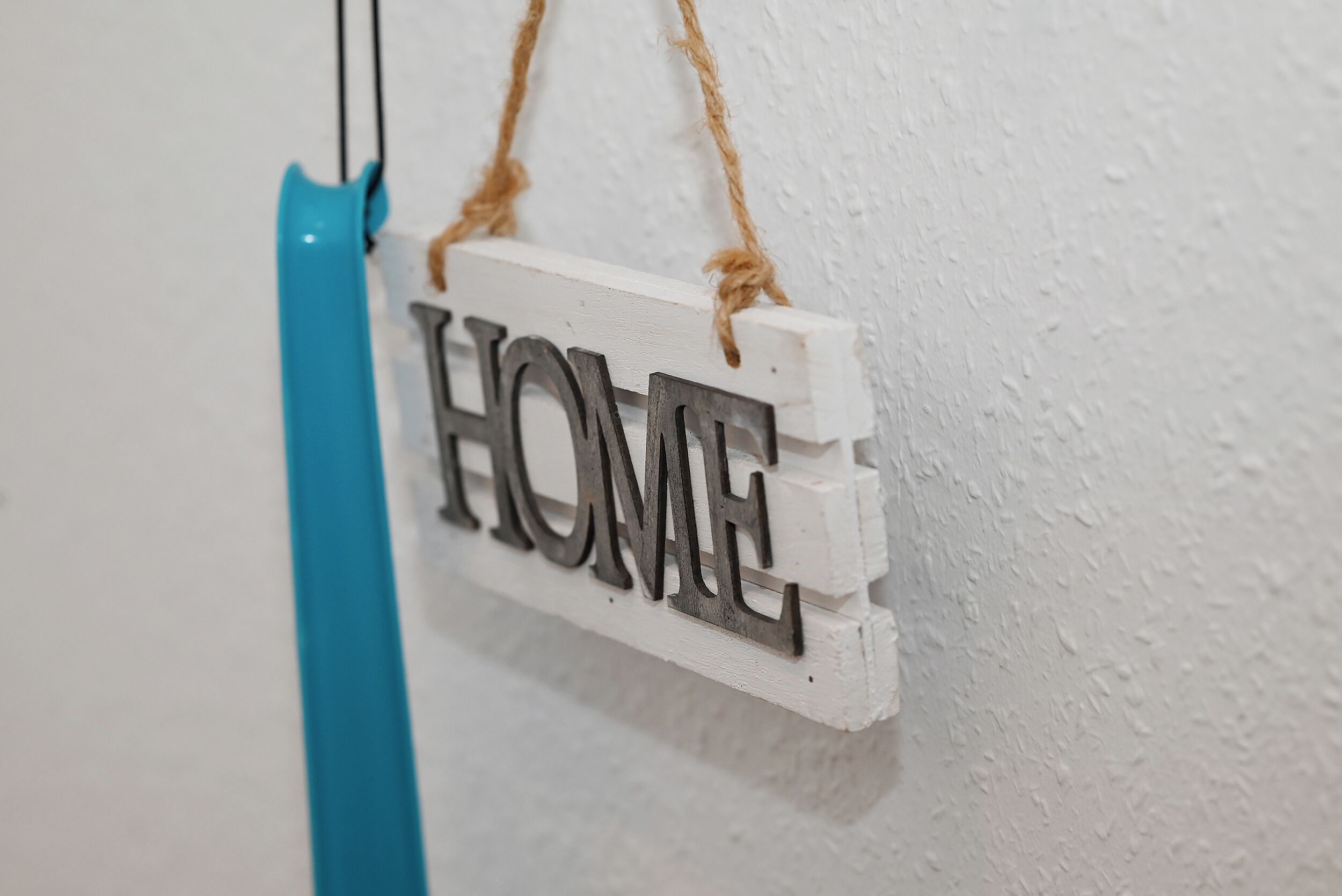 Un letrero de madera blanca con la palabra 'HOME' colgado sobre una pared con textura.