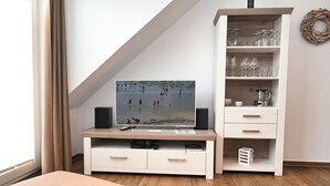 Ein modernes Wohnzimmer mit einem Flachbildfernseher, einer weißen Unterhaltungsanlage mit Regalen und Holzboden.