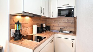 Eine kleine Küche mit weißen Schränken, einem Backofen, einer Kaffeemaschine und einem Spülbecken.