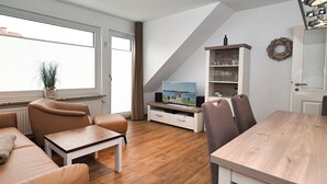 Ein modernes Wohnzimmer mit Holzboden, einer Couch, einem Couchtisch, einem Fernseher und einem Esstisch.