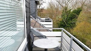Ein Balkon mit kleinem runden Tisch und Stuhl, mit Blick auf einen Garten mit Bäumen und einem Zaun.