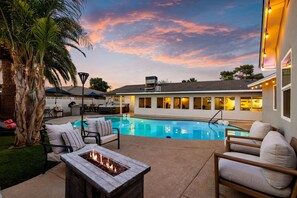 A poolside area with lounge chairs, a fire pit, and a view of the pool.