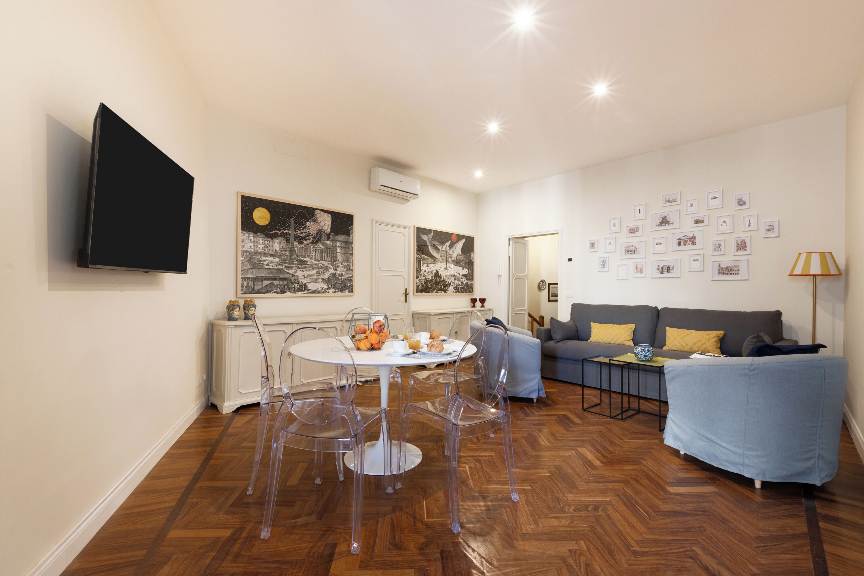 Ein modernes Wohnzimmer mit Esstisch, klaren Stühlen, einem grauen Sofa und einem flachbildfernseher an der Wand.