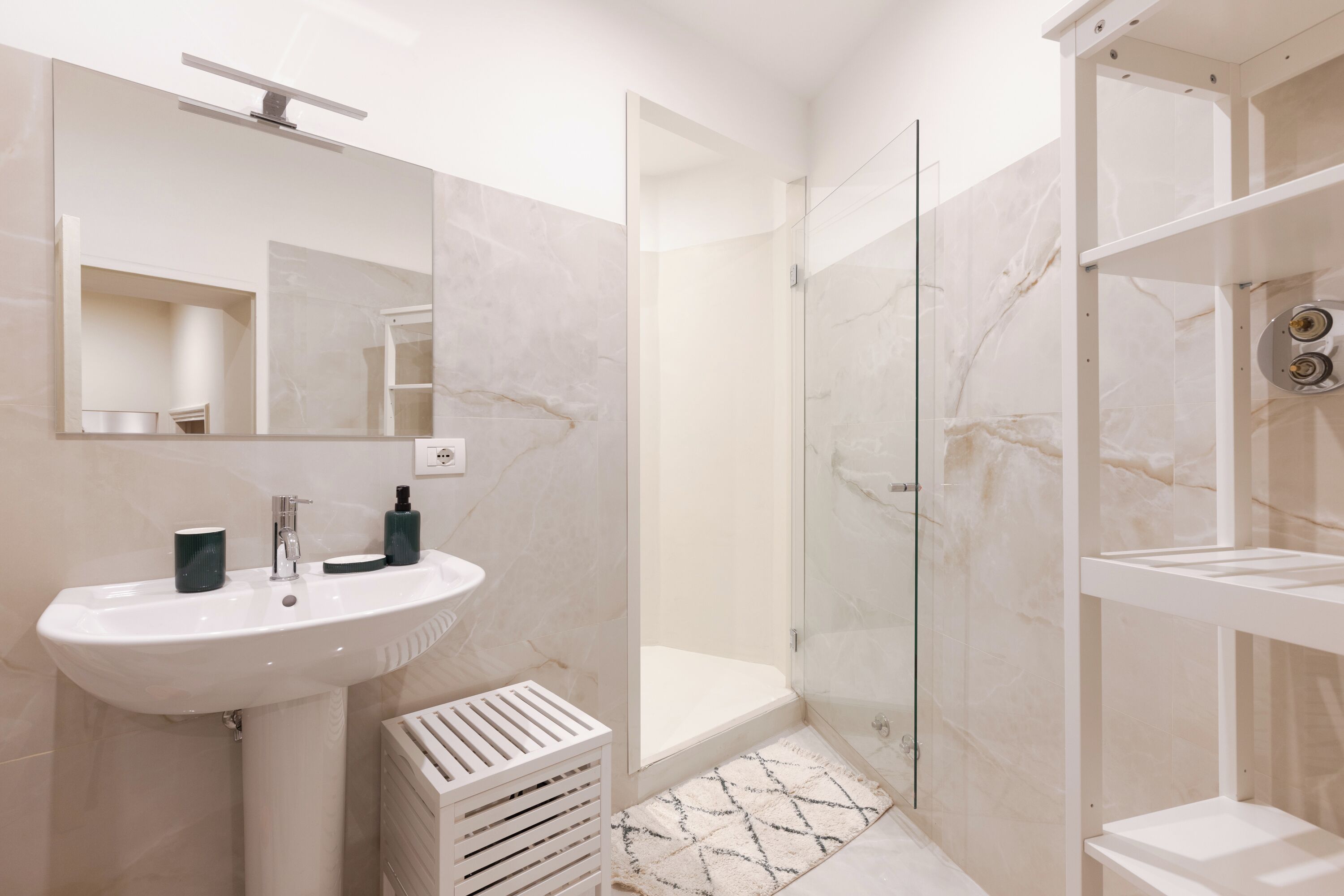 A modern bathroom with a white sink, mirror, and glass shower enclosure.