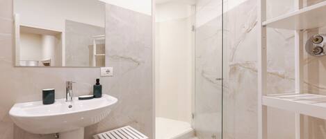 A modern bathroom with a white sink, mirror, and glass shower enclosure.