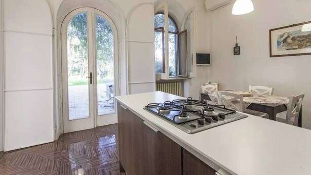 A kitchen with a gas stove, white cabinets, and a dining area with a table and chairs. - Villa Cardinale  in Salento with pinewood and swimming pool. Puglia. (Puglia)