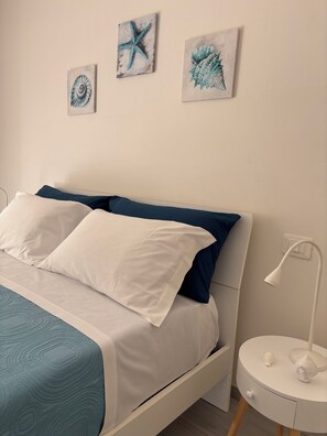 A neatly made bed with white and blue bedding, a bedside table with a lamp, and three wall-mounted artworks depicting sea shells and a starfish. - BlueMare Guests (Polignano a Mare)