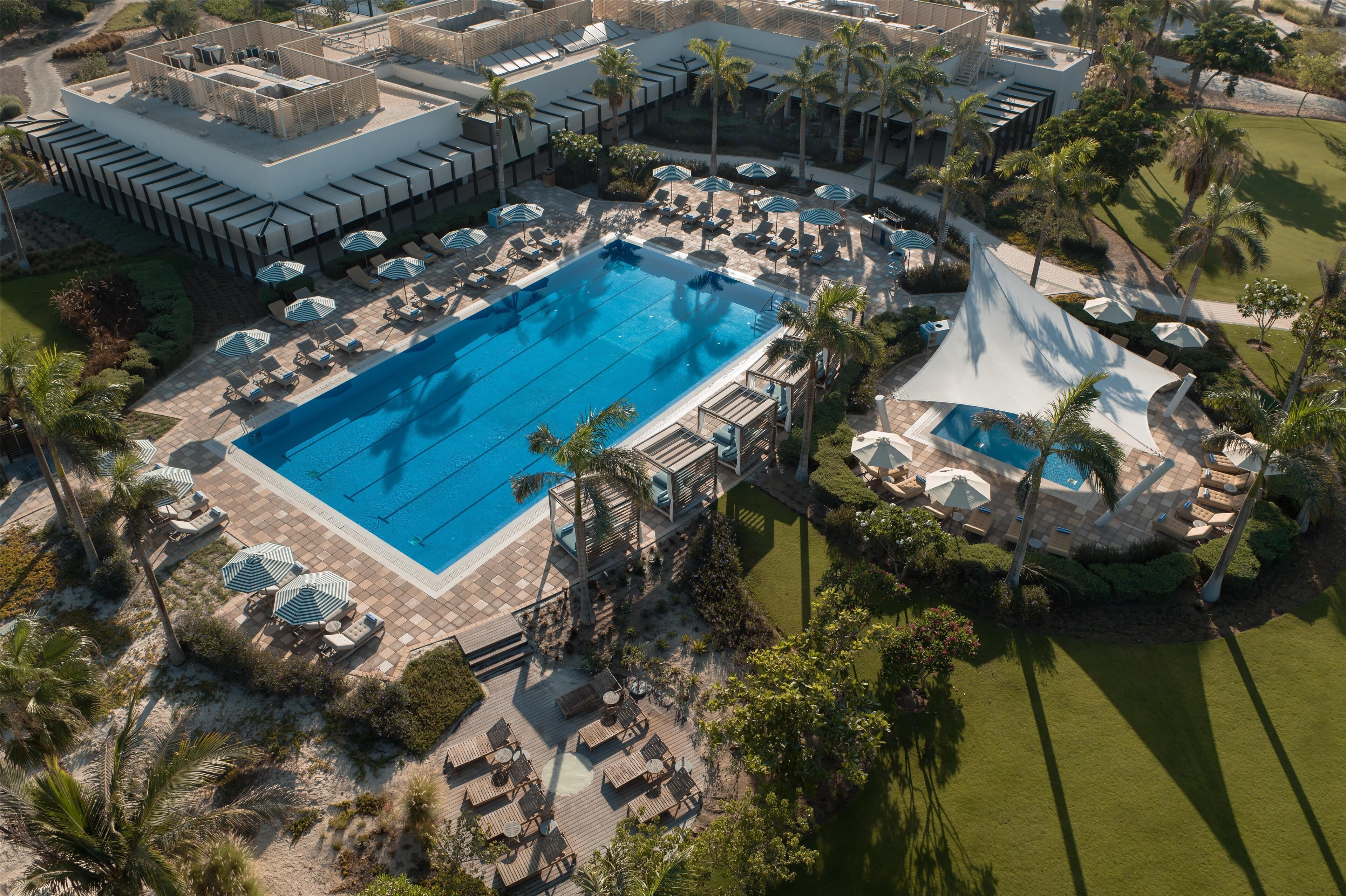 An aerial view of a resort with a large swimming pool, sun loungers, and palm trees.