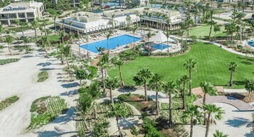 Un resort con varias piscinas, palmeras y un césped bien cuidado.