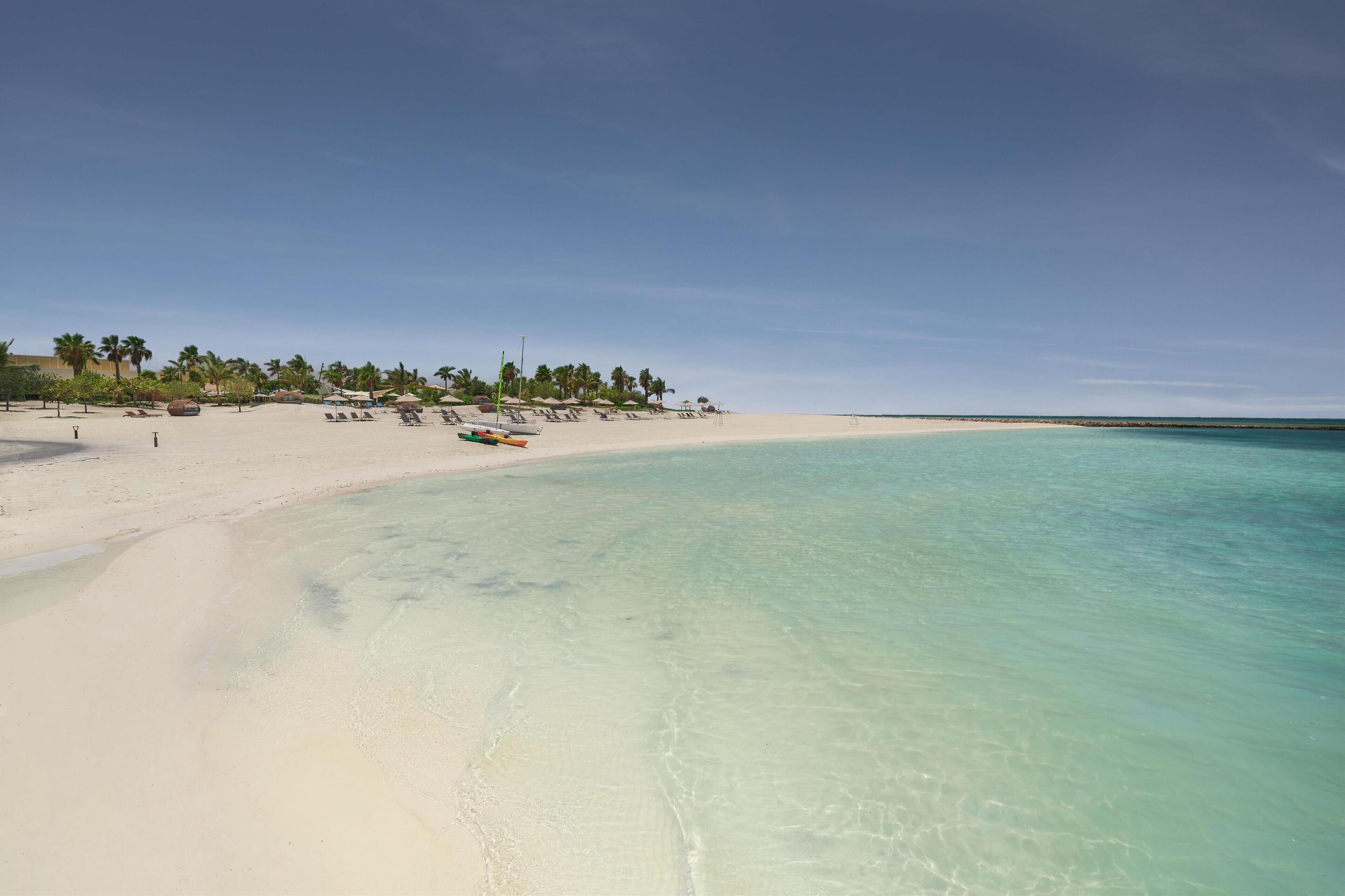 Una playa con agua turquesa cristalina, arena blanca y palmeras.