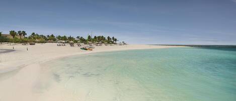Una playa con agua turquesa cristalina, arena blanca y palmeras.