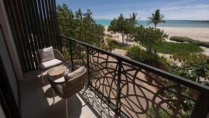 Ein Balkon mit Korbmöbeln und Blick auf einen Strand mit Palmen und einem wolkenlosen Himmel.