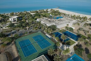 Vista aérea de un resort con cancha de tenis, playa y palmeras.