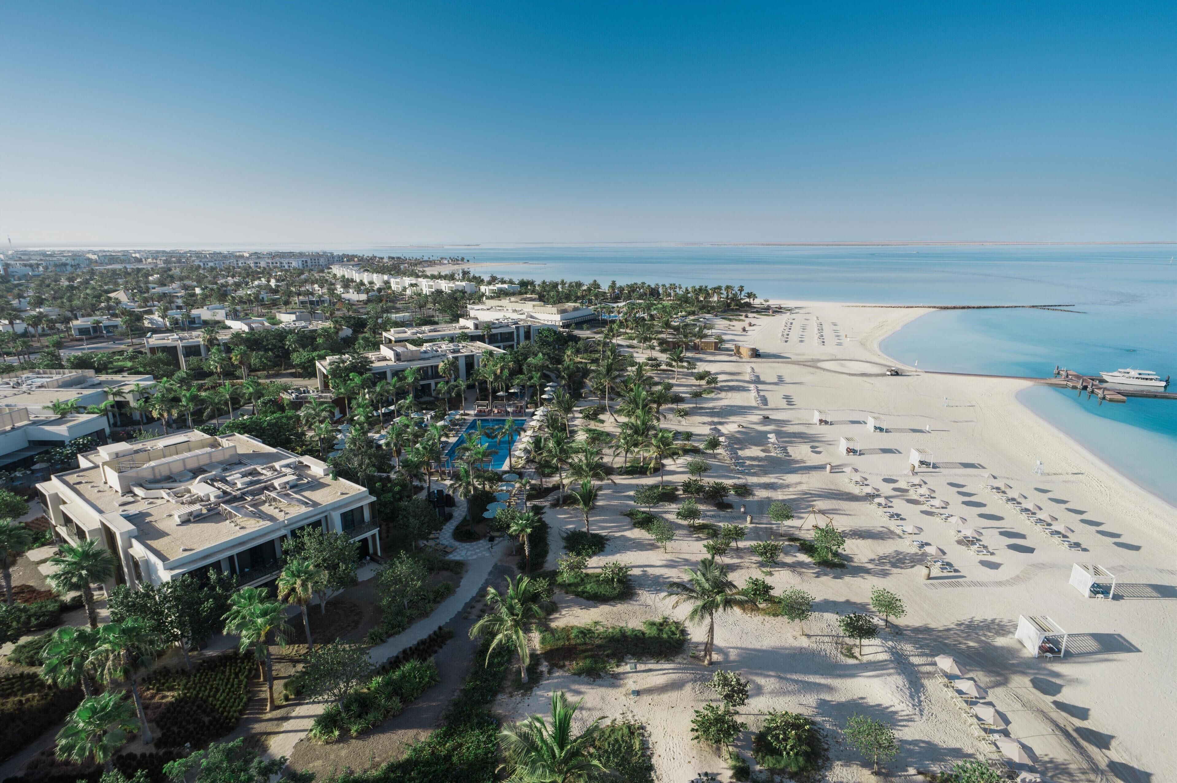 Vue aérienne d’un complexe hôtelier avec une plage, une piscine et des palmiers.