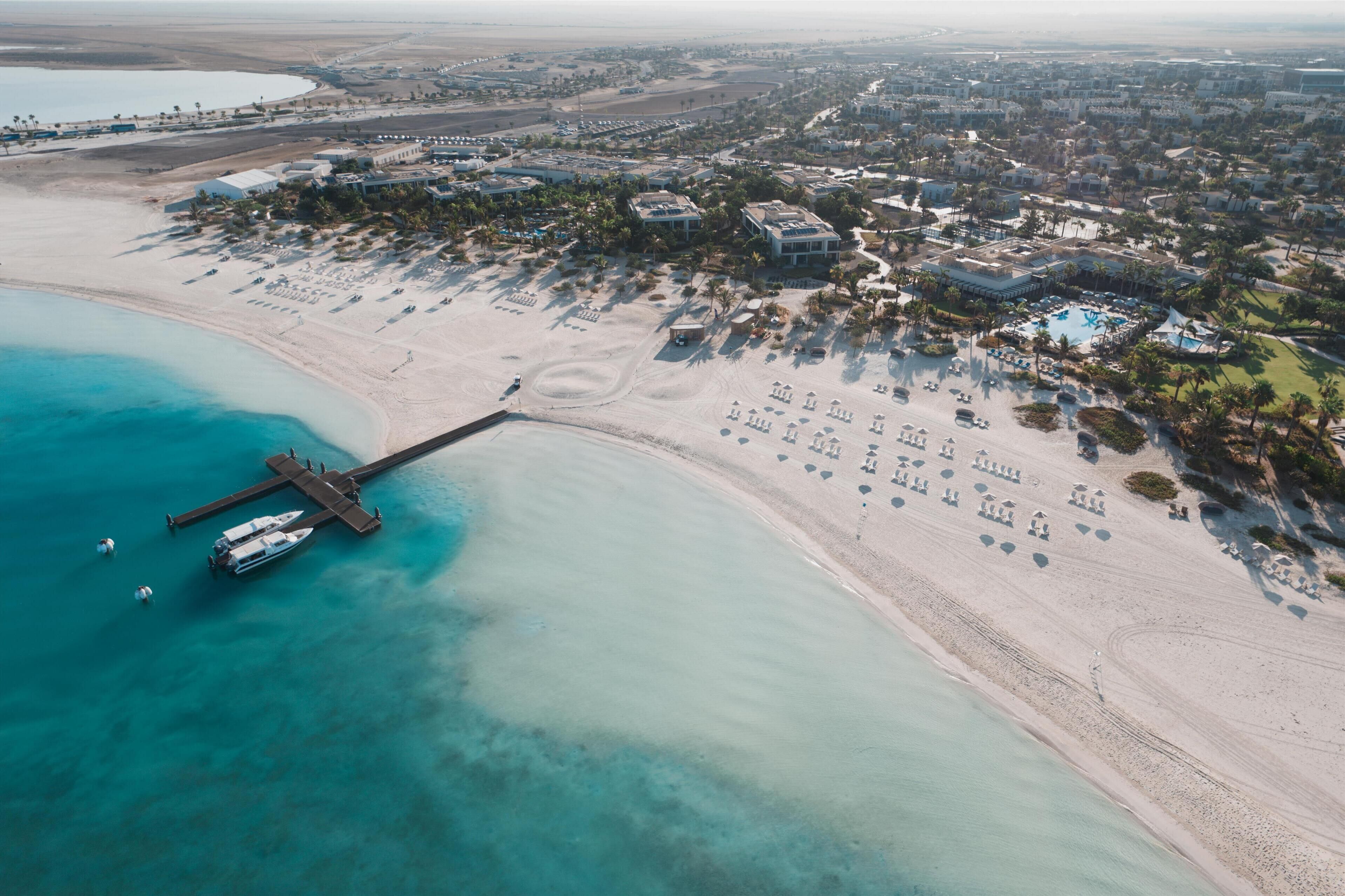 Vista aérea de un balneario costero con muelle, playa y edificios del complejo.