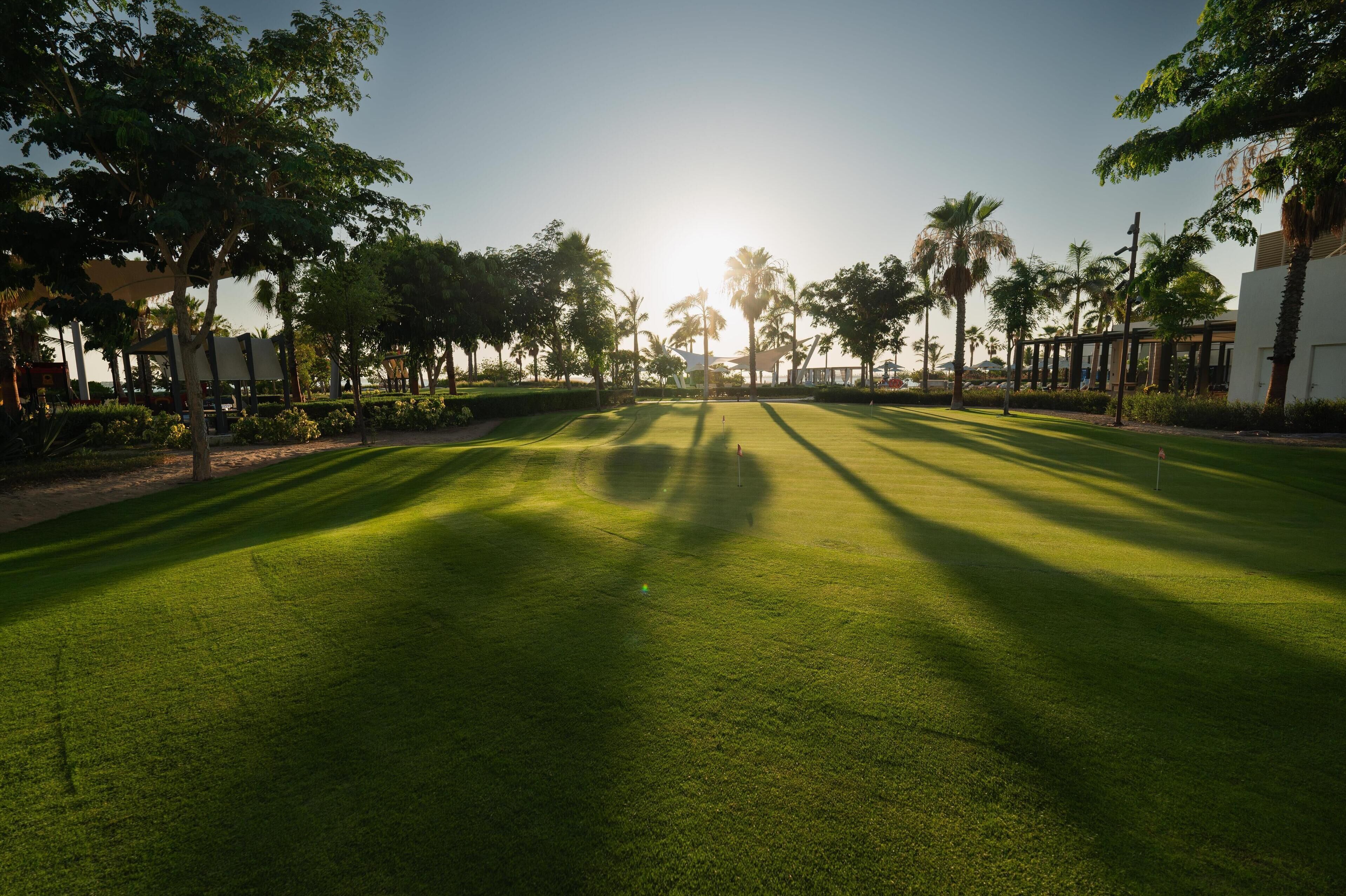 A well-maintained golf course with a clear path, palm trees, and a building in the background.