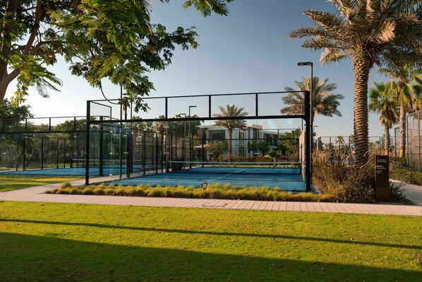 A modern outdoor pool area with a glass enclosure, surrounded by palm trees and a paved walkway. - Turtle Bay Hotel - Red Sea (Umluj)
