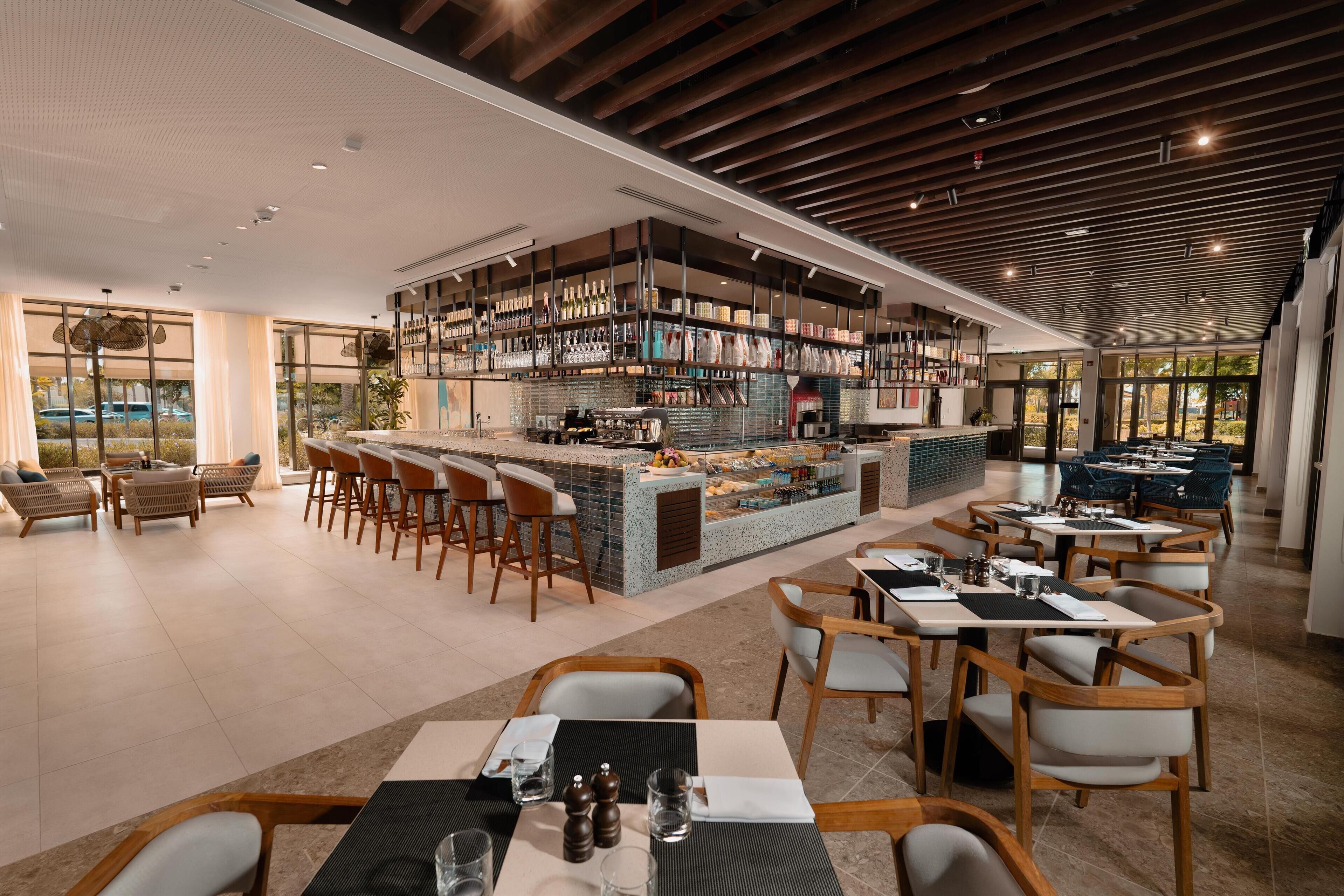 A modern restaurant with a central bar area, multiple seating options, and a view of the outdoors.