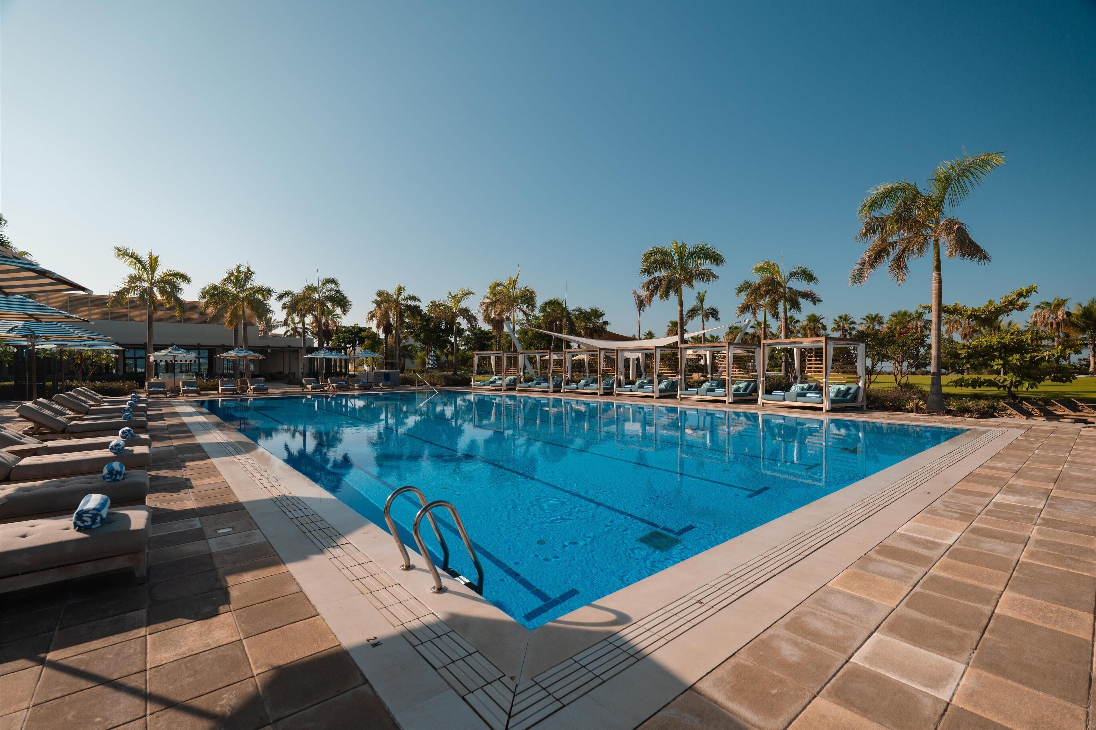A swimming pool with lounge chairs and palm trees.