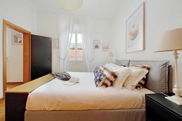 Une chambre à coucher bien rangée, avec un lit, une table de chevet, une lampe et des œuvres d’art accrochées aux murs.