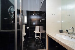 Un baño moderno con cabina de ducha de vidrio, un lavabo blanco y un cuadro en un taburete pequeño.