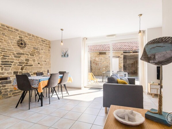 A spacious living area with a stone wall, a dining table with chairs, a sofa, and a cat tree.