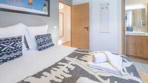 A hotel room with a bed, pillows, a painting, a wooden door, and a bathroom visible through an open door. - Modern 3-bedroom apartment, ski-in/ski-out, perfect for 6 people (Huez)
