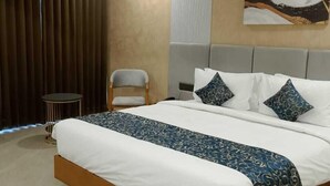 A modern hotel room with a large bed, a chair, a small table, and a ceiling fan. - The Blues Hotel (Sanand)