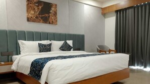 A modern hotel room with a large bed, a grey upholstered headboard, and a wooden nightstand. - The Blues Hotel (Sanand)