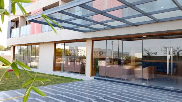 A modern building with large glass windows, a flat roof, and a paved outdoor area. - The Blues Hotel (Sanand)